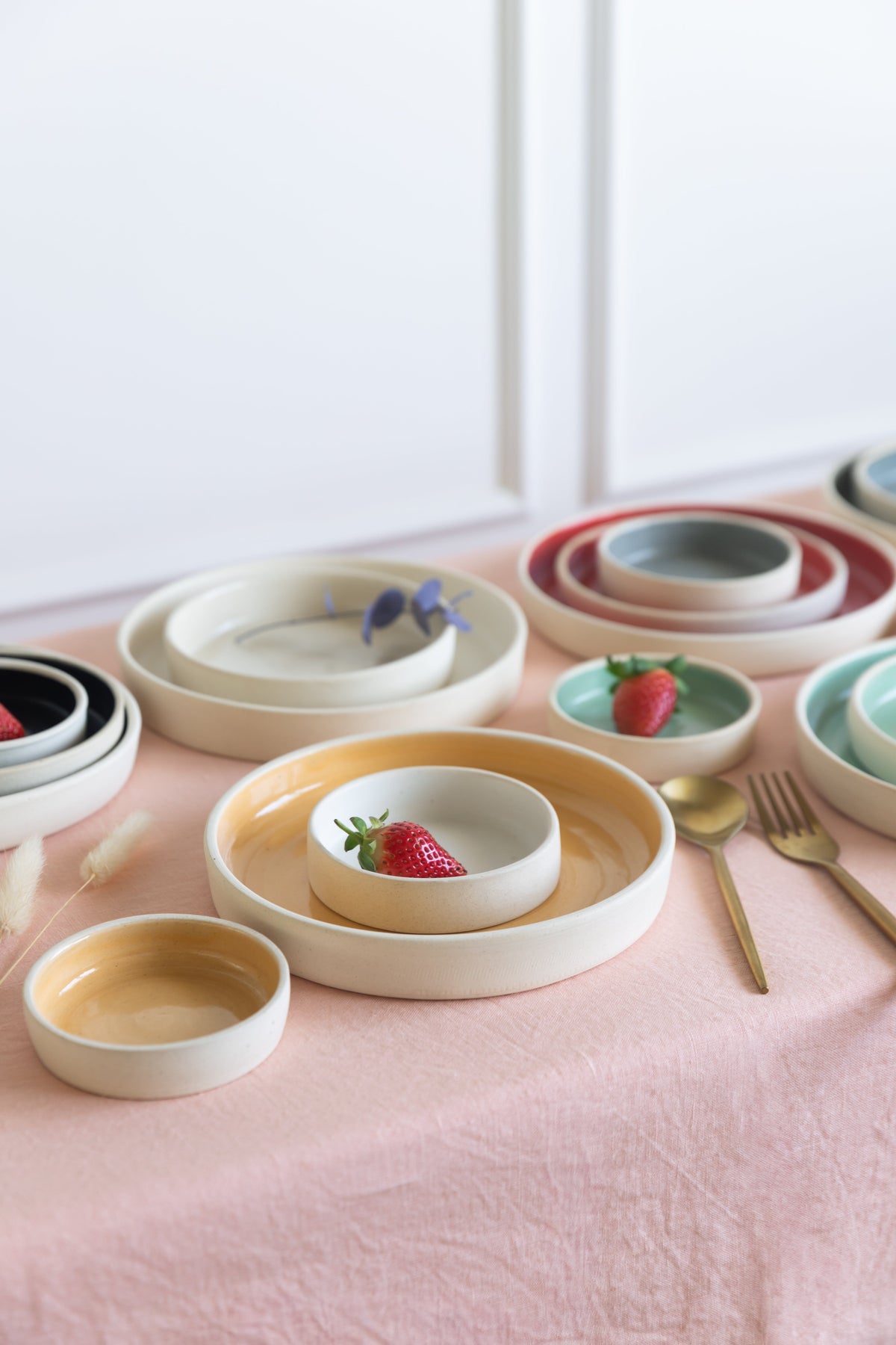 Handmade stoneware raised edge plates in multiple sizes and glaze colours displayed on a table